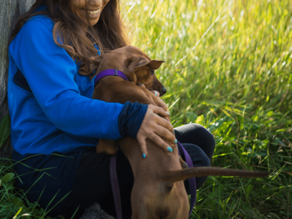 A person pats a dog while sitting in the grass