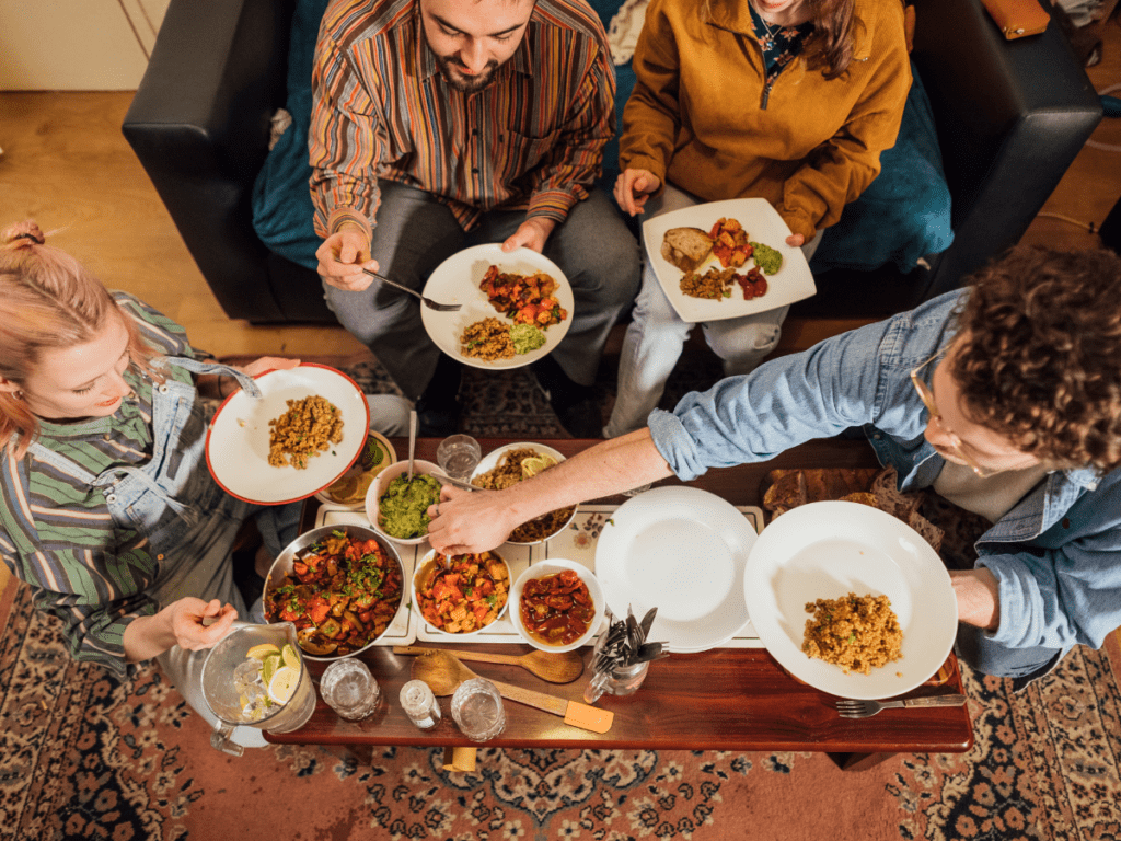 Overhead photo of a group of young adults sharing a family style plant-based meal from a coffee table