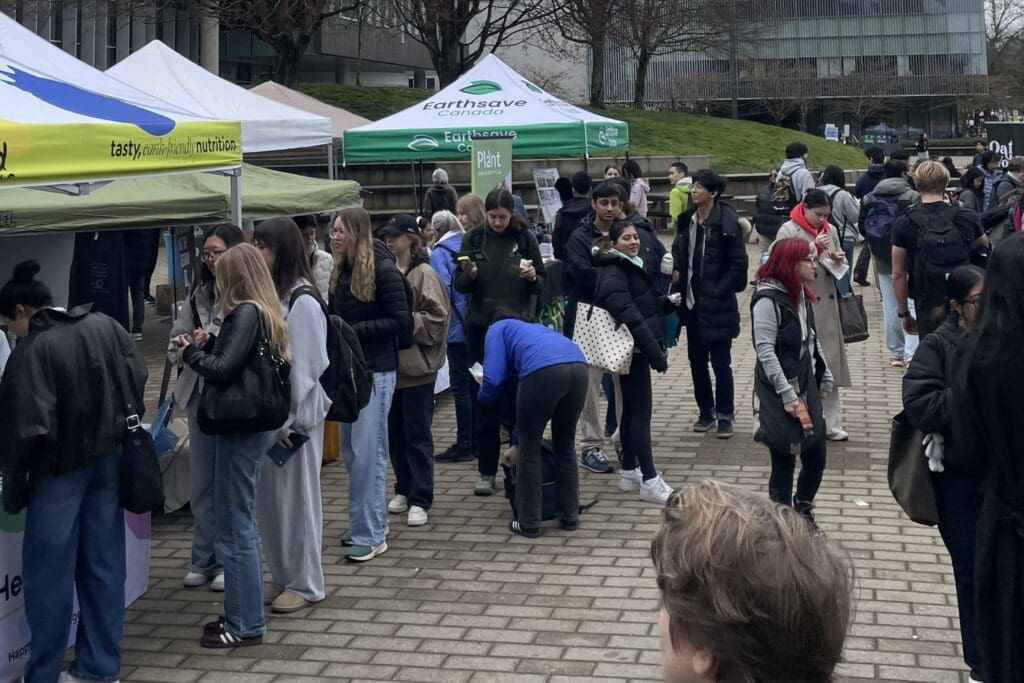 Crowds of students and community members gather outdoors at UBC VegFest, visiting booths and tents hosted by plant-based food brands and advocacy organizations during the campus event.