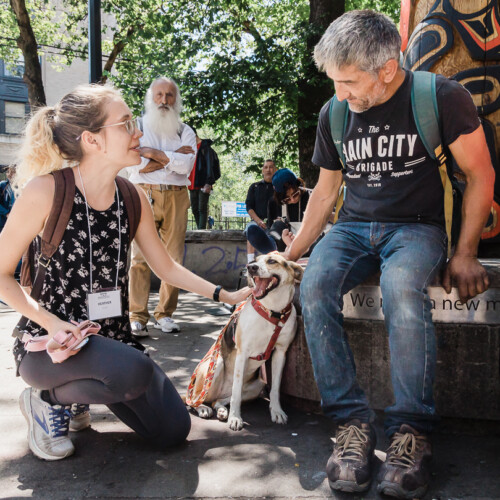 A person kneels down and speaks with a sitting person holding a dog leash.