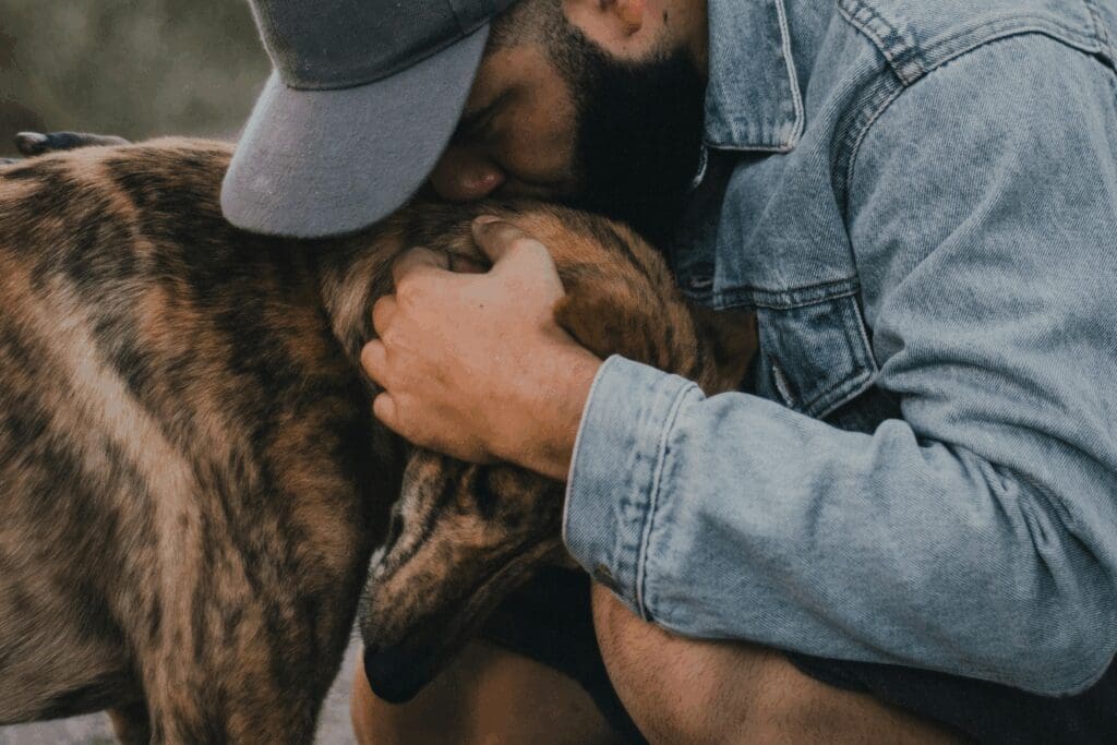A person outdoors cuddling a brown dog