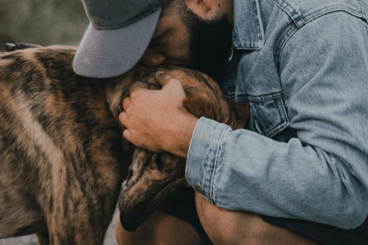 A person outdoors cuddling a brown dog